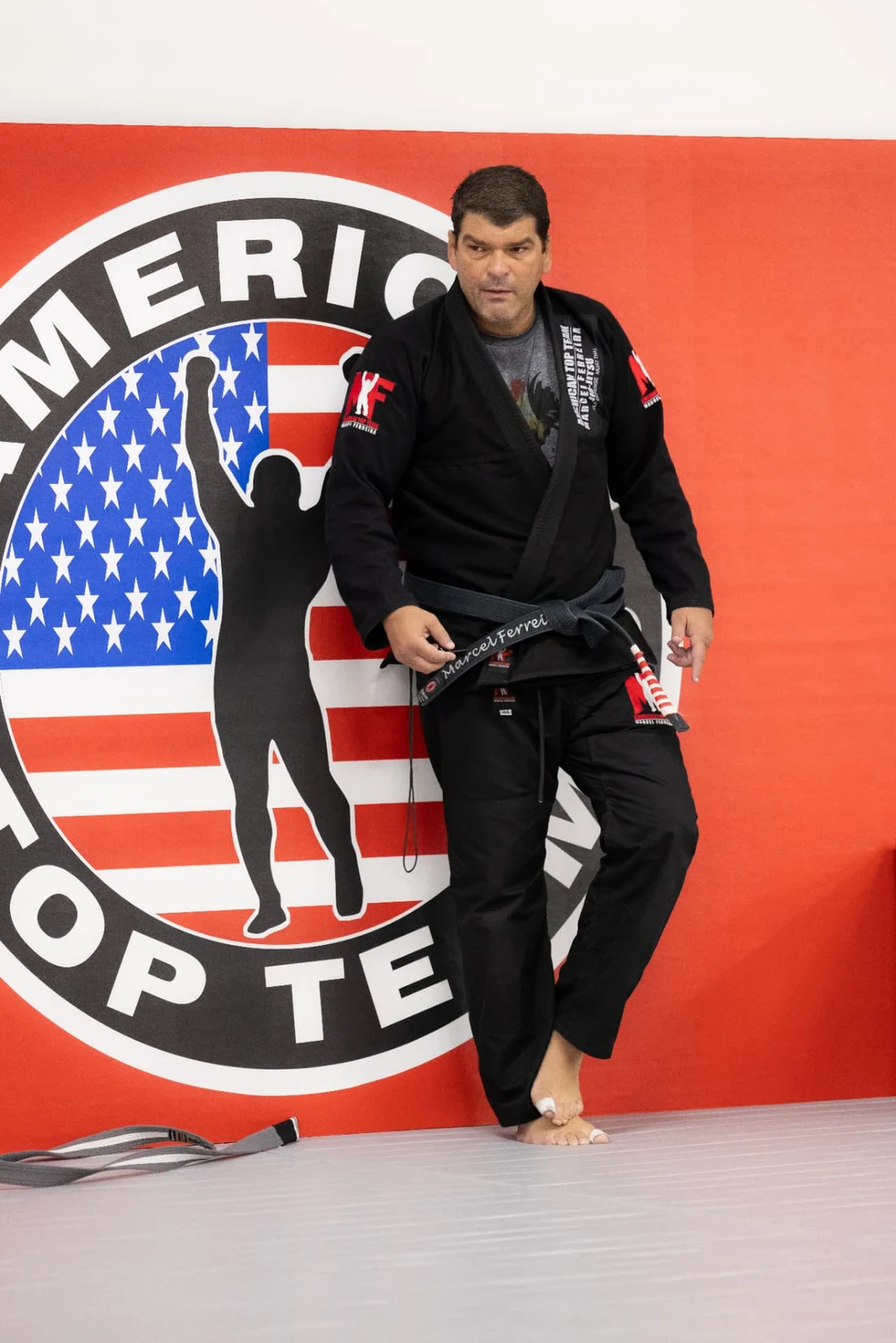 Coach Marcel Ferreira in his black gi and black belt in front of the American Top Team logo wall in Winter Garden